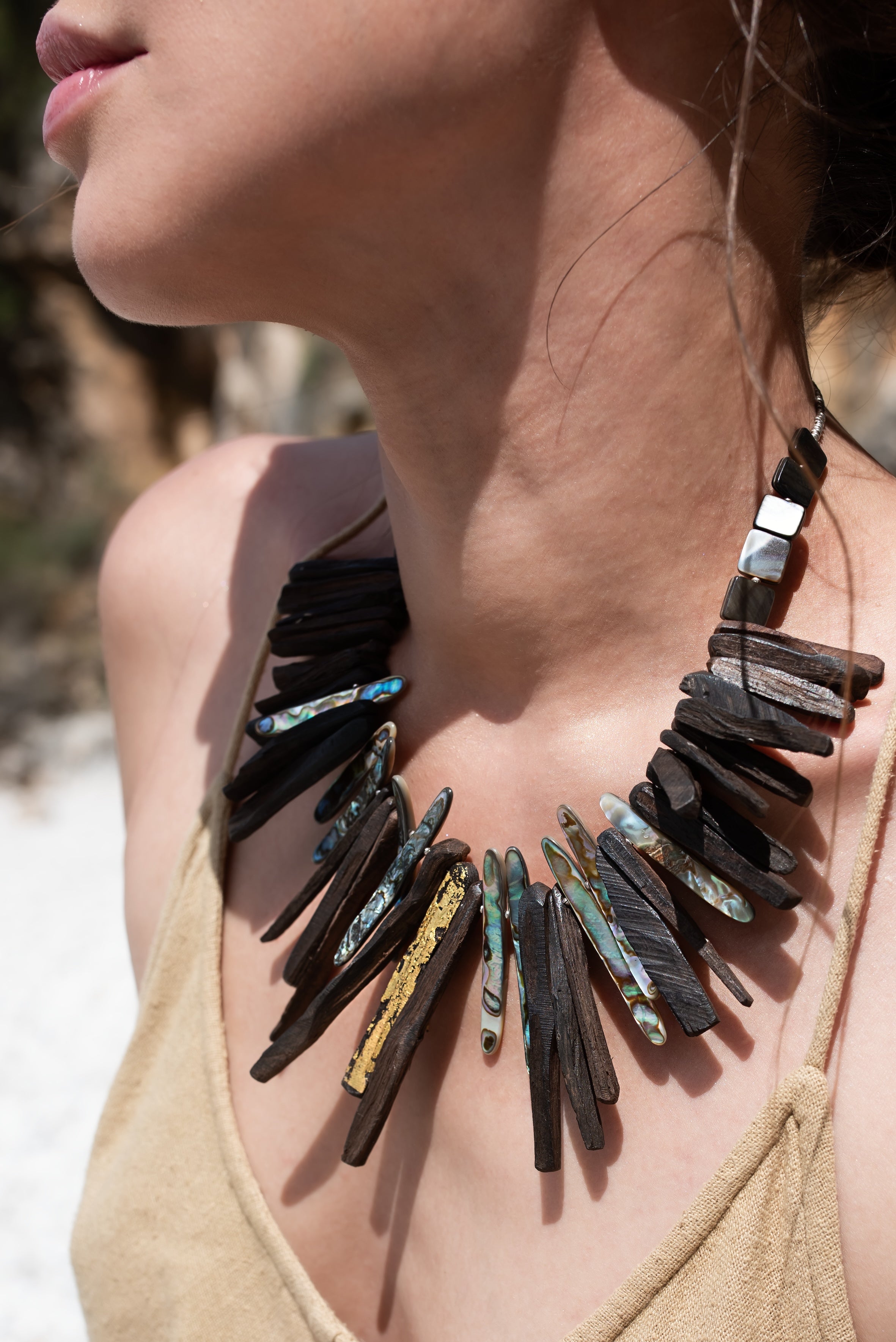 A person wearing a Yaga Statement Necklace which features dark wood elements and sections of mother of pearl.